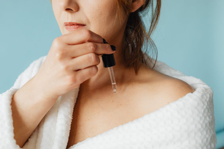 Close-up of a woman in a bathrobe applying serum for skincare routine.
